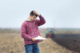 A farmer looking at paperwork in a field.