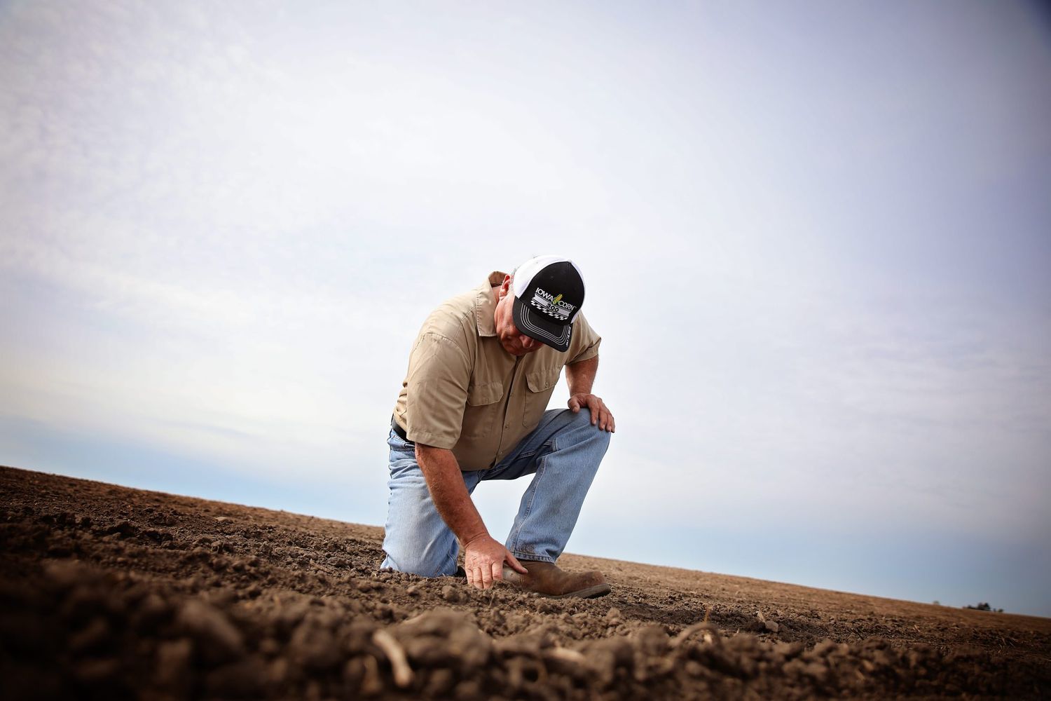 An Iowa farmer kneels to dig in the soil on his farm