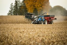 A gray combine unloads corn on the go into a red wagon pulled by a blue tractor at harvest