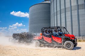 A fully loaded crew of 6 passengers in a red Honda Pioneer 1000-6 Deluxe Crew driving in front of a grain bin.