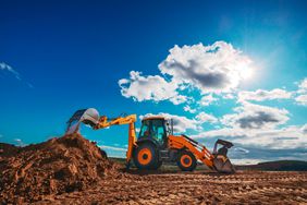 Yellow backhoe loader dumps more dirt onto a pile almost as tall as the machine itself. 