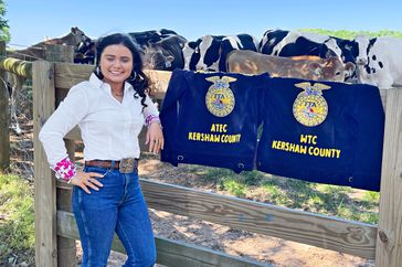 Kinlyn Hinson leans against a fence, also displaying two navy blue FFA jacket.s