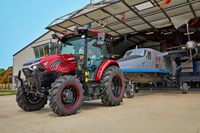 Red Case IH Farmall 75C Electric tractor in front of a small gray airplane. 