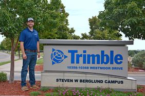 Man in a blue polo and jeans stands next to the Trimble sign at the entrance to their campus. 