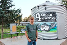 Young man stands in front of a grain bin with signs that read "Gahler Innovations LLC" and "Grain Gyre" 