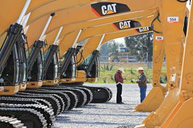 Two men in talking amidst a row of yellow CAT excavators.