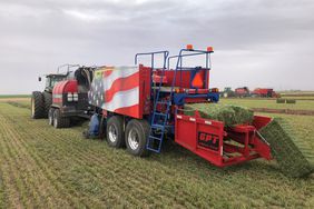 The Twin Pak baler with red paint and American flag packing green hay bales in a field.