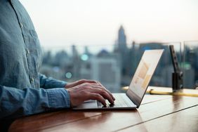 A man's hands working at a laptop computer sitting on a table