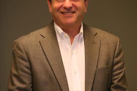 Rich Ansell of Mahindra poses for a portrait wearing a brown suit and white collared shirt