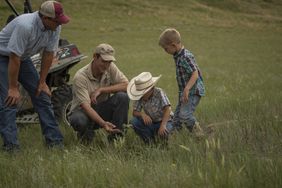 Two men kneel with two young boys to check the pasture