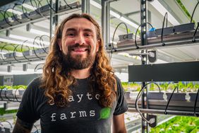 Clayton Mooney stands next to shelves of greens growing inside his Ames, Iowa farm