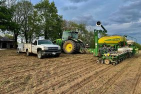 A white Chevy truck and trailer with a green John Deere tractor and planter in the field