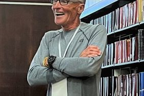 Man in a gray shirt stands in library.