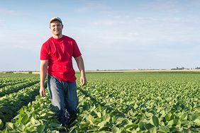 A young farmer smiling in a soybean field.