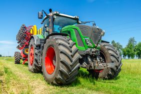 A Fendt tractor pulling a planter through the grassy part of a field.