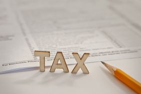 Tax stands in wooden letters in front of a paper tax form with a yellow pencil to the right