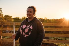 Ashley Bridges McMurry stands on her farm at sunset in a sweatshirt with a pink cow print heart