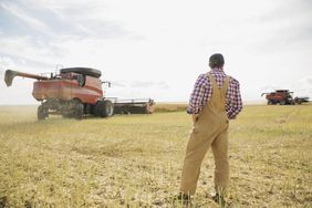 A farmer standing in his field with a combine in the background.