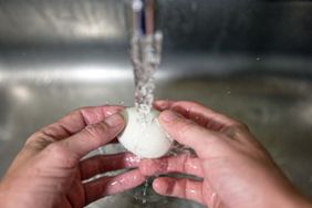 two hands wash fresh egg in steel sink under running water