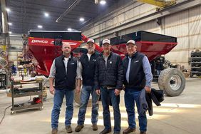 Kelly Garrett, Matt Miles, Chad Henderson, and Kevin Matthews tour Demco with red grain wagons in the background