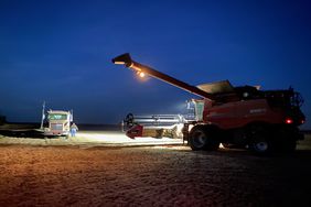 a combine approaches a semi to unload in the dark with lights on