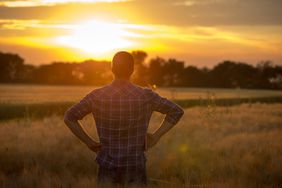 A farmer overlooks his farm as the sunsets.