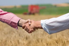 Two farmers shaking hands with a wheat field in the background.