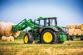 The 2025 John Deere 6M tractor lifting hay bales with the front loader.