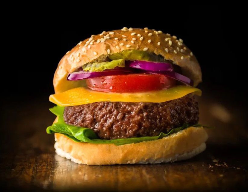 A closeup of a cheeseburger with all the fixings, including lab-grown hamburger.