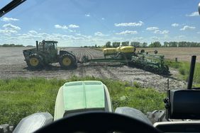 Looking out the windshield of a tractor to the planter and another green tractor on the edge of a field