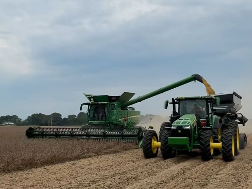 Matt Miles harvests a field of early planted soybeans with a John Deere combine and tractor