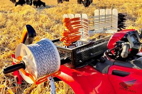 Red 4-wheeler with fencing supplies in front of a pasture of black cattle