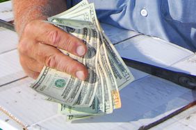 A farmer holding money while sitting at a picnic table.