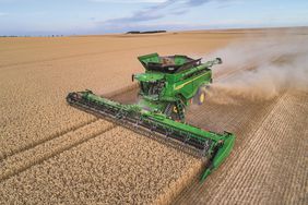 a green John Deere X9 combine harvests a field of wheat in Europe