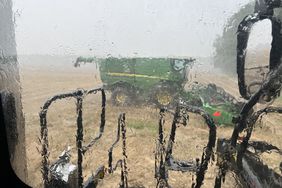 Rain on tractor cab window looking at John Deere combine in a wheat field in Maryland