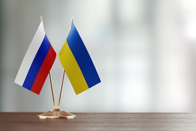 Russian and Ukrainian flag pair on desk over defocused background.