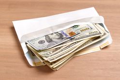 A white envelope of U.S. cash sitting on a wood table