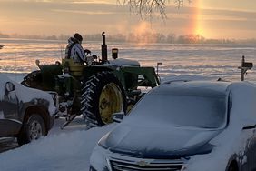 A sundog hovers on the horizon as Jerry Nelson uses his John Deere â3010â tractor to clear snow after a recent prairie blizzard.