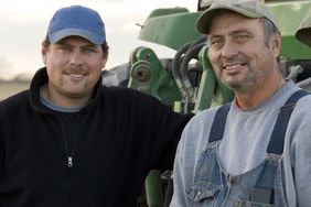 Two smiling farmers stand next to a tractor.