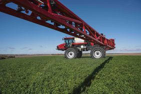 A red Case IH sprayer in a field with red, Specialty Enterprises sprayer arms.