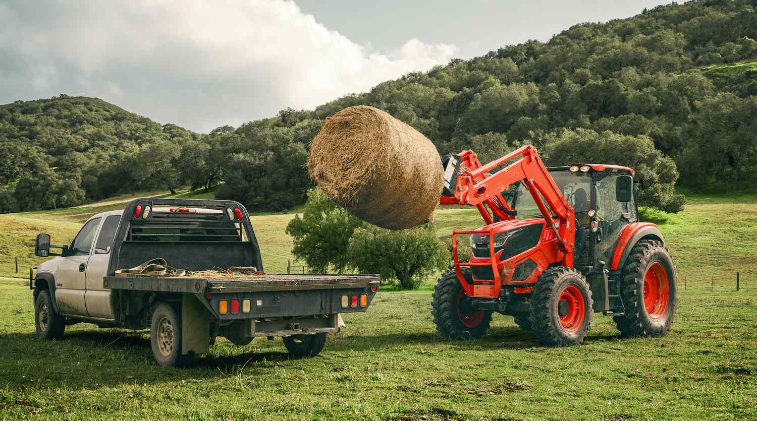 The Kioti HX Series tractor loading a round bale of hay on to a flat bed truck.