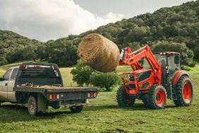 The Kioti HX Series tractor loading a round bale of hay on to a flat bed truck.