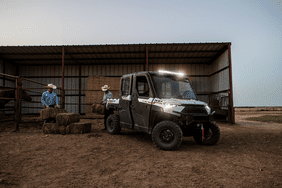 Two farmers in a stable loading the back of the Polaris Ranger UTV.