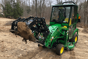 The Iron Fist Grapple mounted to a John Deere tractor, with the loader raised and holding a large rock.