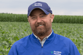 Jason Webster of Precision Planting, standing in a field with blue Precision Planting hat and shirt.