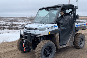 Zach Johnson drives a white and blue Polaris Ranger XP Kinetic on a gravel road in Minnesota