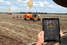 Robot machinery in a field with a person using a tablet to control them.